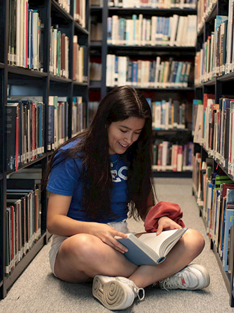 Joven leyendo un libro en una biblioteca