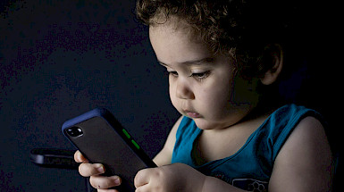 Infante sostiene y observa un teléfono móvil.