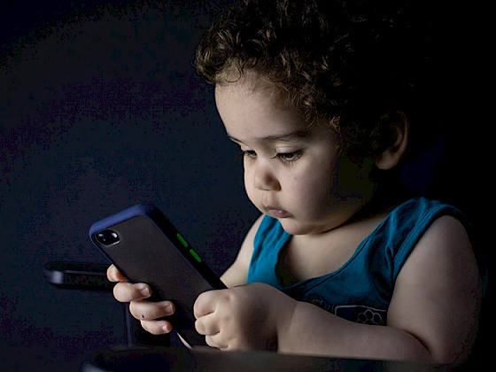 Infante sostiene y observa un teléfono móvil.