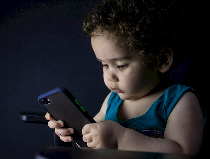Infante sostiene y observa un teléfono móvil.