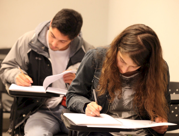 Dos estudiantes, un hombre y una mujer, tomando apuntes en una sala de clases.