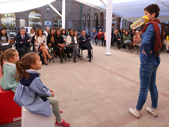 Tres niños haciendo una representación teatral frente a un público en un patio.