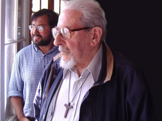 Sacerdote Beltrán Villegas mira por una ventana junto a otra persona.