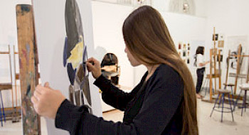 Una mujer pintando sobre un lienzo, en una sala de pintura.