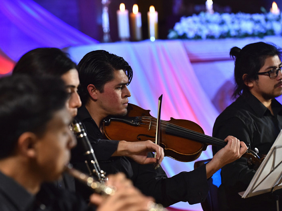 Hombres tocando instrumentos, de primer plano se ve a uno tocando un violin.