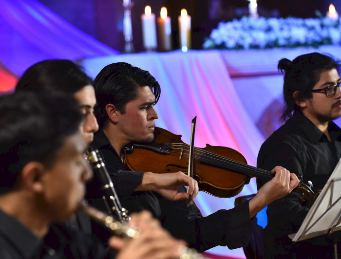 Hombres tocando instrumentos, de primer plano se ve a uno tocando un violin.