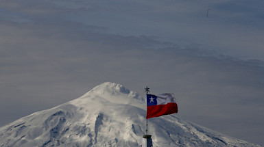 Vista del volcán Villarrica nevado con una bandera chilena al frente.