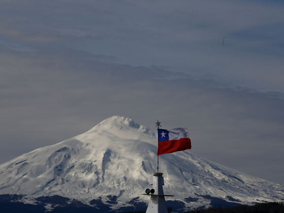 Vista del volcán Villarrica nevado con una bandera chilena al frente.