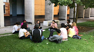 Estudiantes conversando, sentados en círculo sobre el pasto.