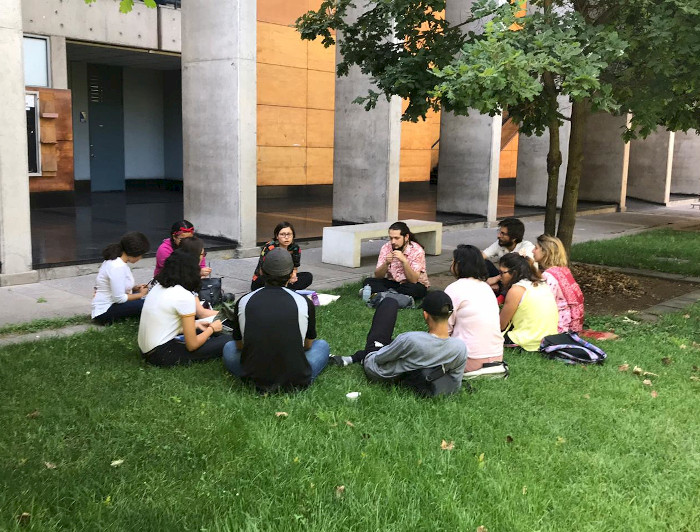 Estudiantes conversando, sentados en círculo sobre el pasto.