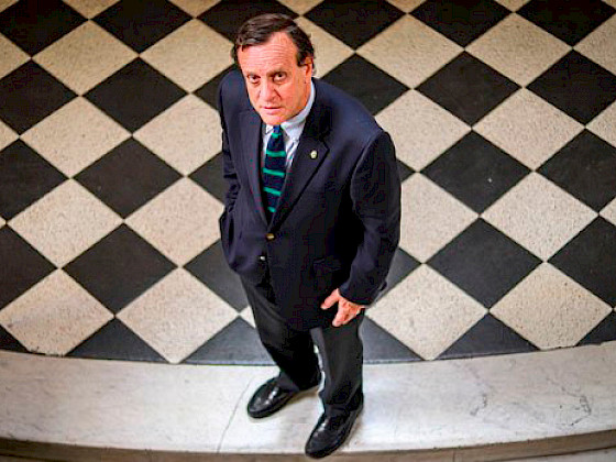 Rector Ignacio Sánchez mira hacia arriba de pie sobre un fondo de baldosas negras y blancas.