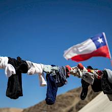 Ropa tendida contra cielo azul y bandera chilena. (Foto: Karina Fuenzalida)