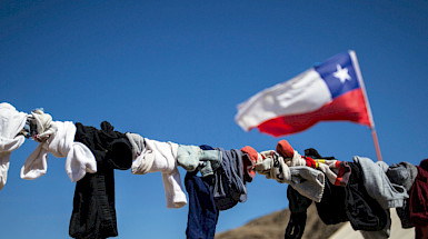 Ropa tendida contra cielo azul y bandera chilena. (Foto: Karina Fuenzalida)