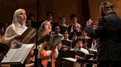 Coro de hombres y mujeres frente a un maestro de orquesta. Fotografía: Escuela de Ingeniería.