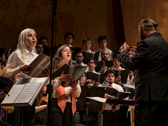 Coro de hombres y mujeres frente a un maestro de orquesta. Fotografía: Escuela de Ingeniería.