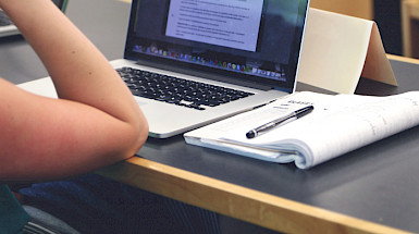 Estudiante mirando un computador con cuaderno al lado.