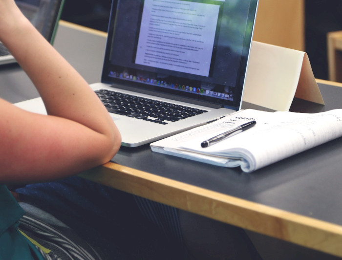 Estudiante mirando un computador con cuaderno al lado.