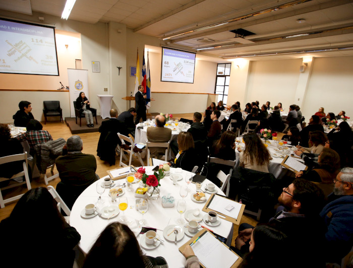 Grupo de personas sentadas en una mesa con café y galletas, escuchando al rector Ignacio Sánchez. Fotografía: César Cortés