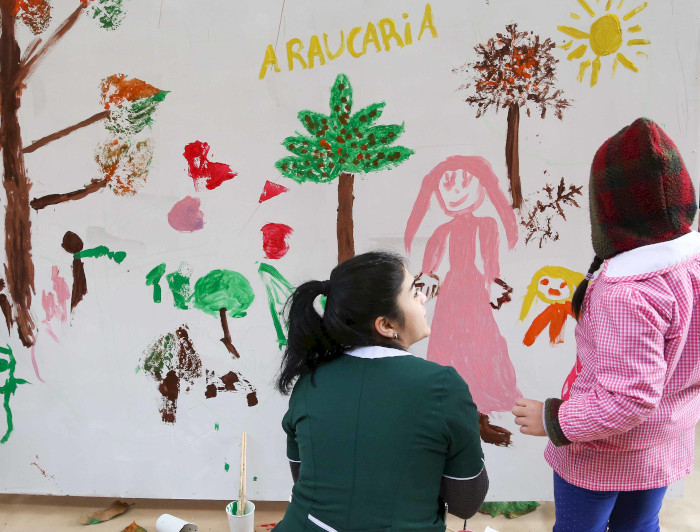 Profesora y niña miran mural pintado por niños.