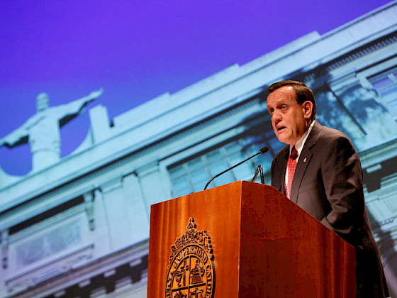 El rector Ignacio Sánchez hablando en un podio, con una imagen del Cristo de Casa Central detrás de él.