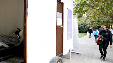 Una persona mirando los siestarios instalados en el campus San Joaquín, mientras hay un siestario abierto con una persona durmiendo adentro. Fotografía: Karina Fuenzalida.