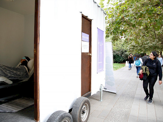 Una persona mirando los siestarios instalados en el campus San Joaquín, mientras hay un siestario abierto con una persona durmiendo adentro. Fotografía: Karina Fuenzalida.