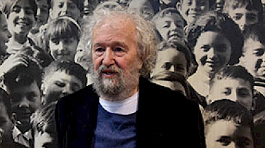 Tomás Moulián posa frente a una foto llena de niños.