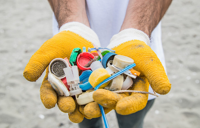 Ucéanos has collected more than 5 tons of waste and debris, mainly plastic, with cleanups. In this pictures two gloved hands showing plastic debris collected on a beach: caps, straws, and strings (Photo: Ucéanos)
