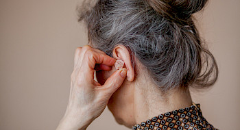 Se visualiza mujer adulto mayor poniéndose un audífono en la oreja.