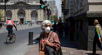 Mujer, persona mayor, pelo canoso, de frente, caminando en el centro de Santiago, usando mascarilla blanca.