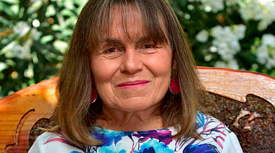 Fotografía de perfil de Patricia May con un respaldo de madera y vegetación de fondo
