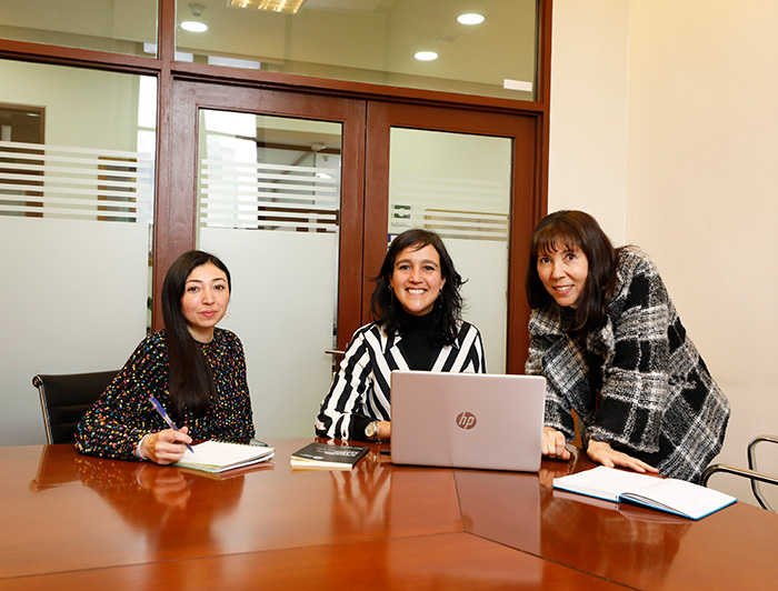 Equipo de la Dirección de Equidad de Género en una mesa de reuniones trabajando junto a un computador.