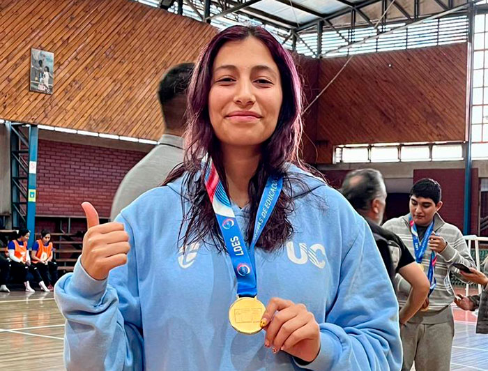 Natalia Gutiérrez usando un poltrón de la UC y mostrando una medalla, en un gimnasio.