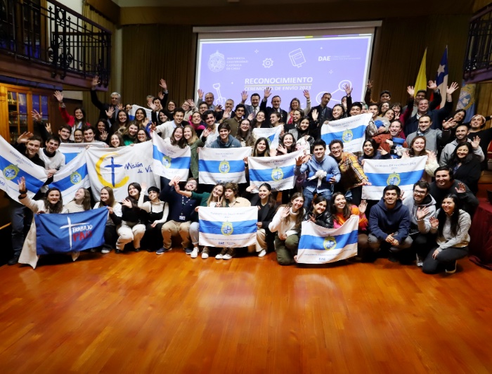 Estudiantes sostienen banderas de la UC y de misiones, durante una ceremonia de envío de trabajos voluntarios.