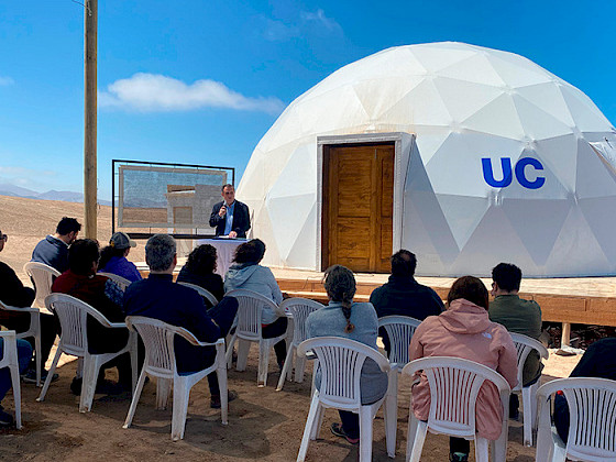 UC Chile President Ignacio Sánchez next to a white dome with the UC Chile logo and a scale model of a fog catcher.