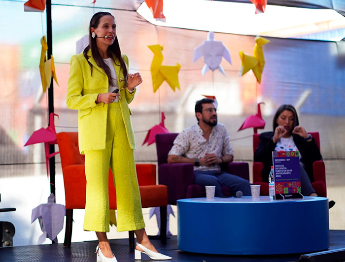 La neurocientífica Florencia Álamos, vestida de amarillo, hace su presentación en el escenario de Puerto de Ideas; de fondo, dos de sus colegas.