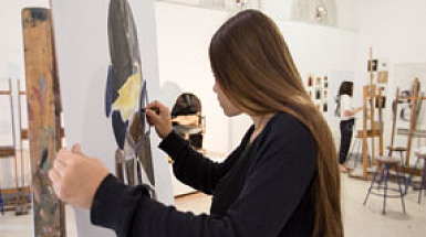 Una mujer pintando sobre un lienzo, en una sala de pintura.