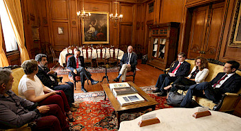 Grupo de personas sentadas, con una mesa al centro. Fotografía: César Cortés.