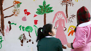 Profesora y niña miran mural pintado por niños.